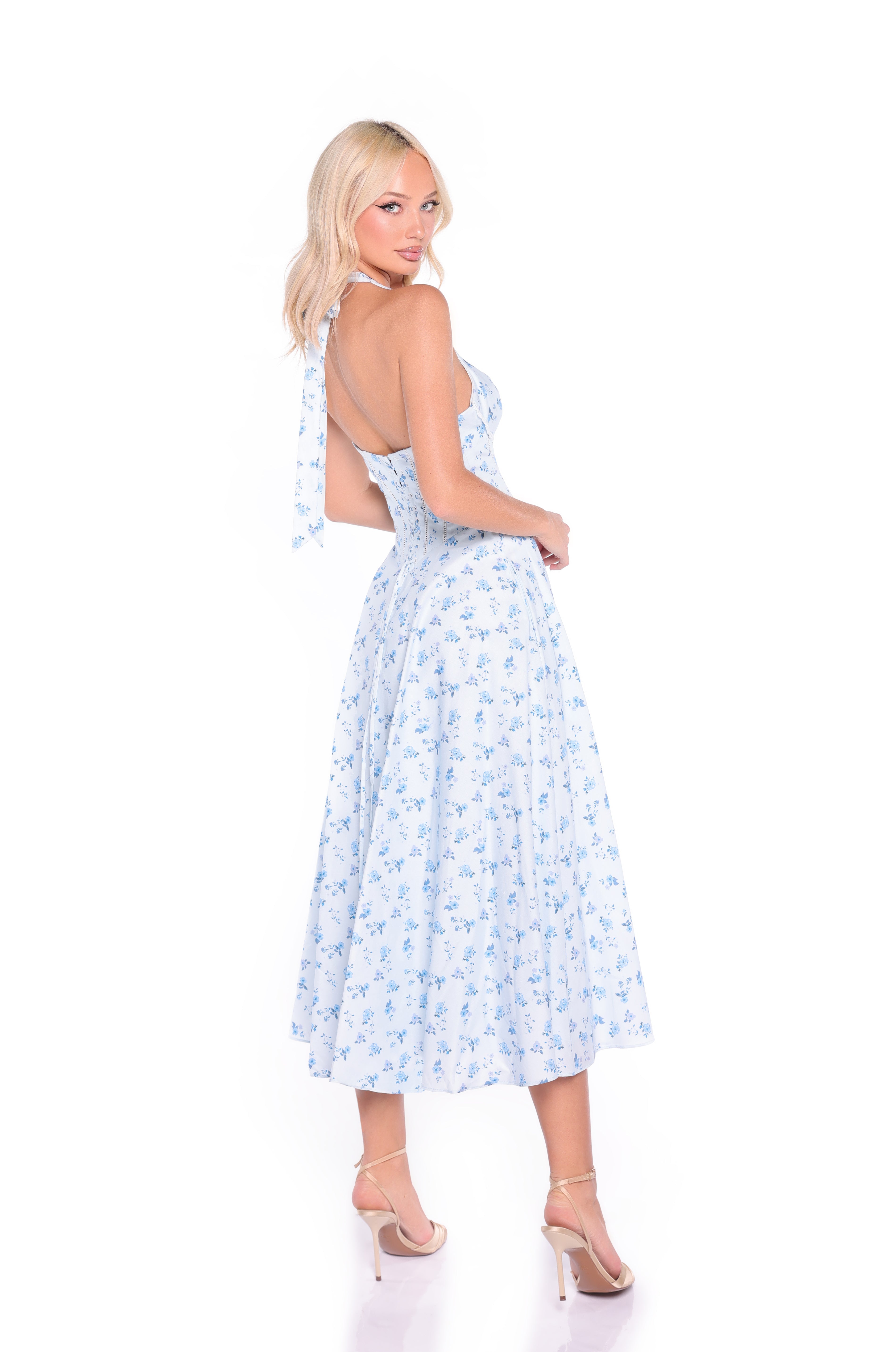 A woman models the Light Blue Floral Halter Summer Midi Dress: Eliza, standing in high heels and facing slightly backward against a white background.
